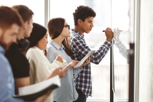 Students writing algebra equations on whiteboard in classroom