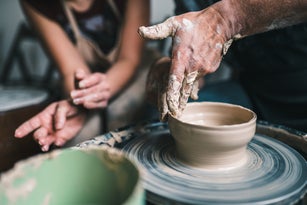 Young woman instructor teaching a man to do pottery using a pottery wheel on a workshop