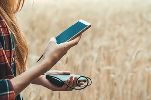 Girl in a yellow field holding a phone in her hand, and charging it from power bank.