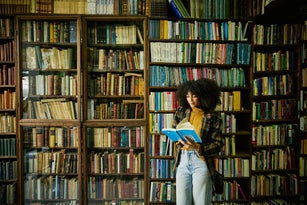Wide shot woman reading book while browsing in antique bookstore