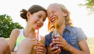 Laughing girls drinking juice outdoors