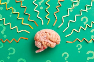A human brain model with folded paper brainwaves and question marks