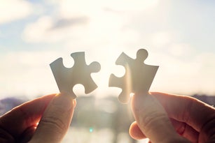 Hands trying to fit two puzzle pieces together