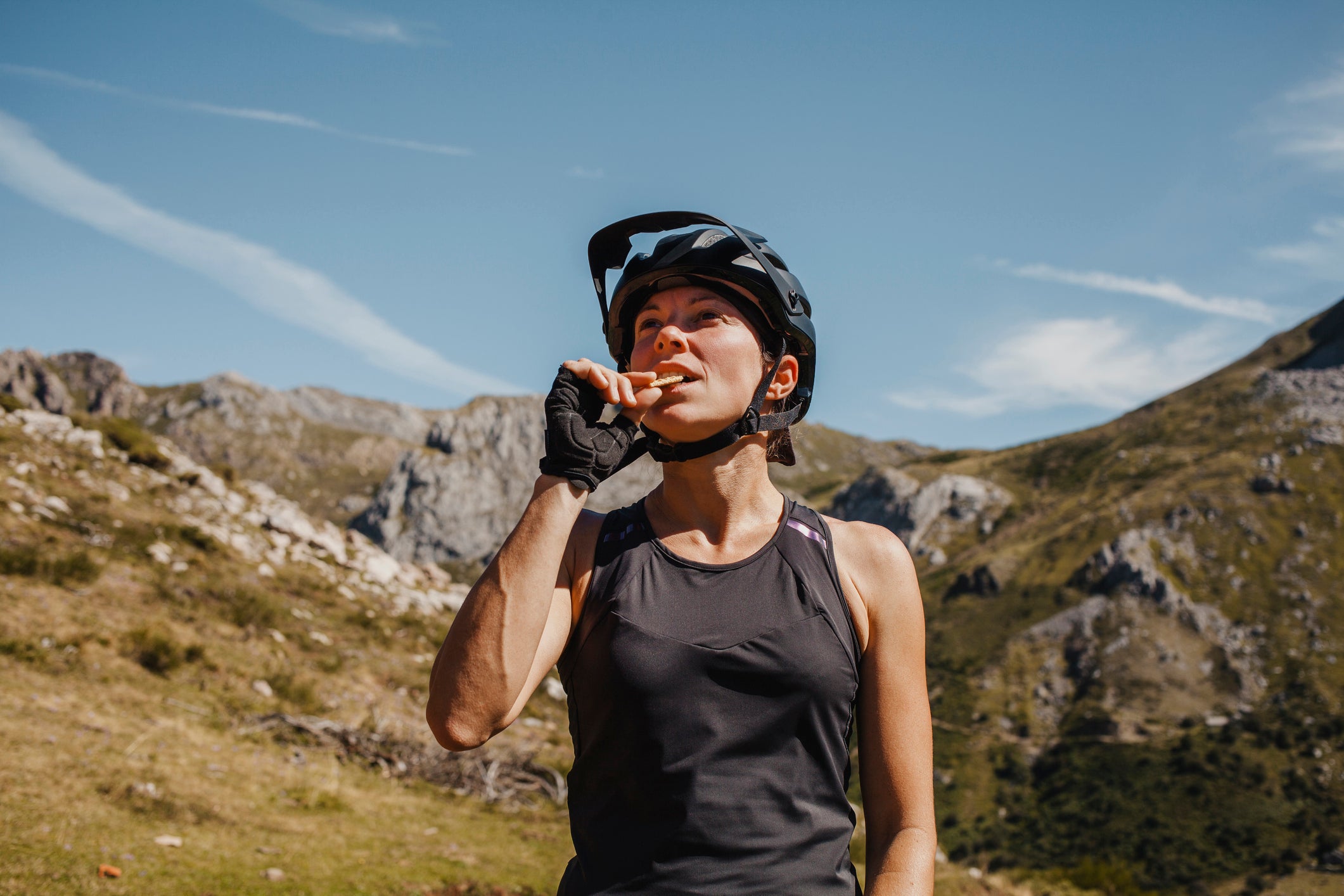 Woman wearing cycling helmet eating biscuit while standing against mountain at Somiedo Natural park, Spain