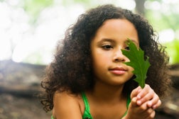 young girl staring intently at a green leaf