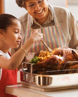 Hispanic granddaughter helping grandmother baste turkey