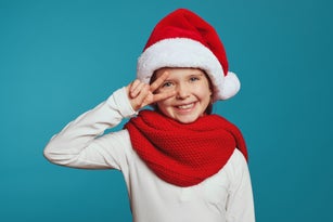 Cheerful little girl wearing christmas hat and red scarf, showing peace gesture