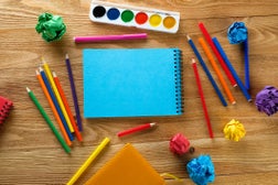 Colored markers and pencils, a blank drawing pad, watercolor paints on a wooden table. Topics of children's creativity, school and preschool education, hobbies. Copy space. Drawing lessons. Back to school.
