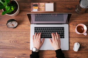 Woman's hands working on laptop at home office, top view