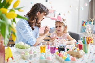 Woman painting daughters nose while painting easter eggs at table