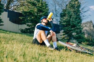 Cyclist drinking from water bottle while resting on grassy hillside