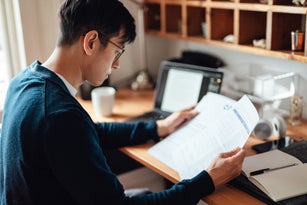Young Asian man looking at financial bills while working on laptop at home
