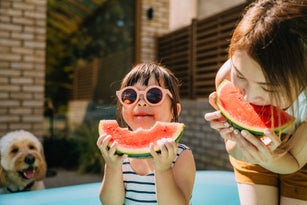 Young Asian toddler girl refreshing with  watermelon slice with her mother in backyard
