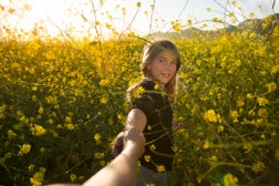 Girl pulling her mother into a yellow field of mustard wildflowers
