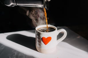 Hot coffee being poured into a white mug with red heart