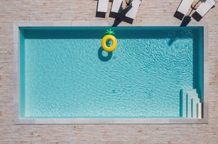 Empty rectangular blue swimming pool with sunbeds and umbrellas and big inflatable Yellow Pineapple floating tube. Rent a real estate or Chill out summer vacation in luxury resorts concept.