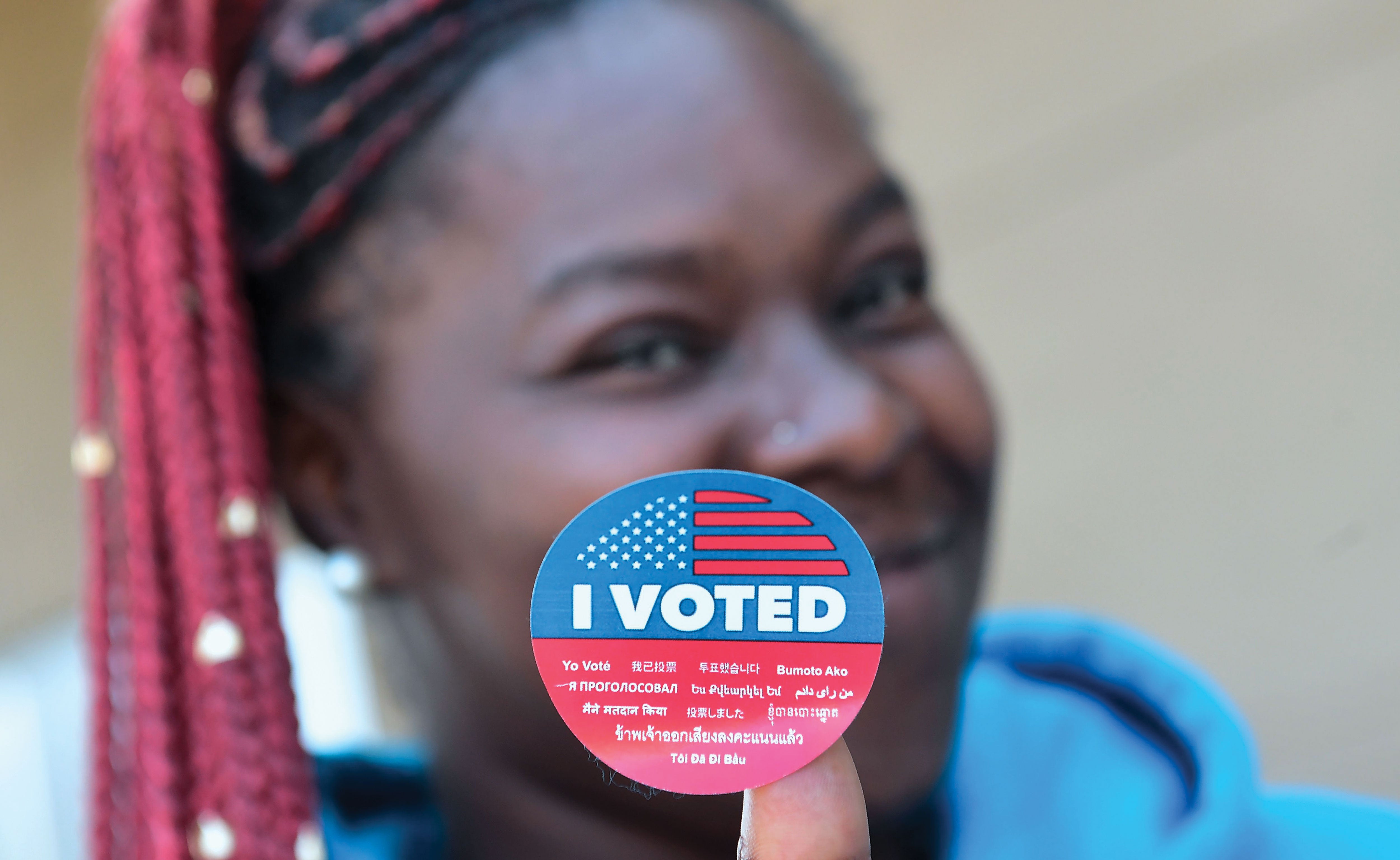 Young woman holding an I Voted sticker up to the camera.