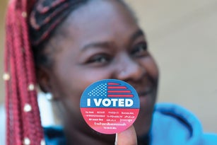 Young woman holding an I Voted sticker up to the camera.