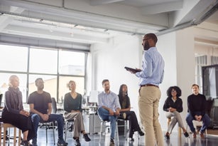 African businessman stands at the front and engaging with colleagues seated for a meeting