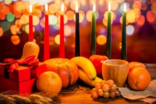 Kwanzaa holiday concept with decorate seven candles red, black and green, gift box, pumpkin, bowl and fruit on light blur bokeh background