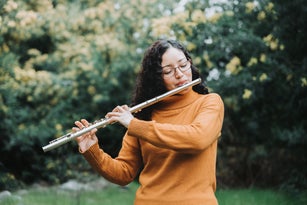 Curly brunette woman with glasses playing transverse flute outdoor in nature