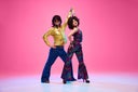 Groovy dance couple in bright attire performing disco moves in motion against gradient pink studio background.