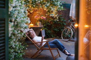 Woman relaxing on deck chair in backyard at dusk, reading on digital tablet