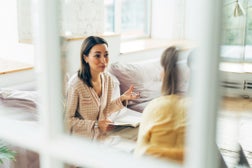 Two women in armchairs and talking. Reflection in the mirror