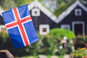 Iceland, Iceland national flag in the foreground, typical icelandic houses with grass on the roof in the background