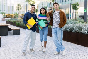 Three young diverse student friends smiling at camera standing together at university campus. Inclusion, diversity and authentic people concept.