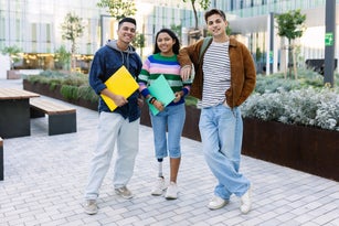 Three young diverse student friends smiling at camera standing together at university campus. Inclusion, diversity and authentic people concept.