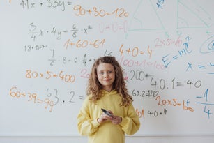 Little girl standing in front of school board, mathematic class.