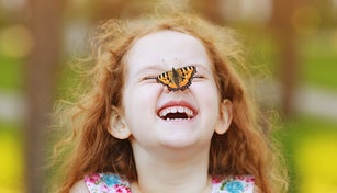 Funny laughing curly girl with a butterfly on his nose.