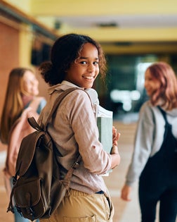 Happy black teenage girl in high school hallway looking at camera.