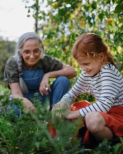 Grandmother with granddaughter working in garden together.