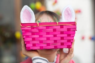 Child (6-7) hiding face behind pink Easter basket and rabbit ears
