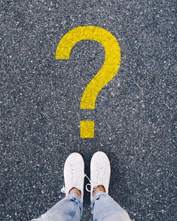 "Person standing in front of a yellow question mark symbol painted on asphalt