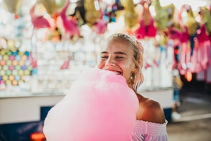 Close-up of smiling young woman with eyes closed holding cotton candy at amusement park