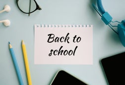 School and office supplies over blue background. Back to School concept. Pencils, crayons, headphones, phone, easel and eyeglasses.