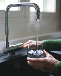 Close up of a senior woman's hand filling a glass of filtered water right from the tap in the kitchen sink at home