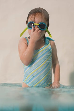 Girl (3-5) standing in swimming pool, wearing goggles and holding nose