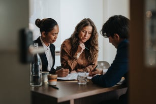 Young businessman writing while discussing strategy with female colleagues sitting at desk in office