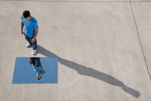 Man standing with mirror on ground and reflection