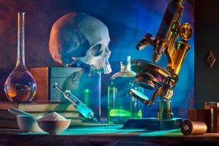 Old medicine research concept. History of science, alchemy, vaccination. Horror film style. Microscope, human skull, syringe with vaccine, laboratory glassware in smoke.