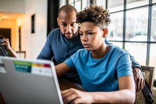 Father helping teenage son with homework in residential kitchen