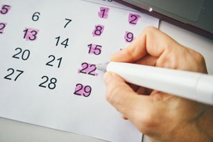 Person Highlighting Important Dates on a Calendar with a Marker