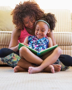 Mixed race mother and daughter reading book on floor near sofa