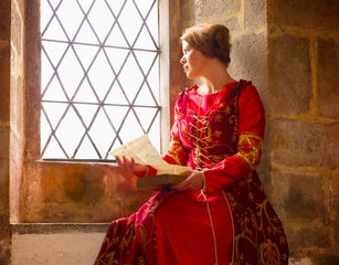 Caucasian woman in medieval costume reading at castle window