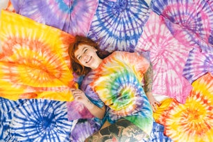 Cheerful young woman lies surrounded by tai-dai textiles