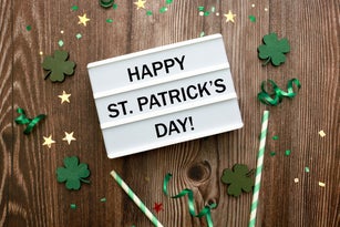 Lightbox with text. Green clover confetti over brown wooden background. Card for St Patrick's Day with copy space for text.